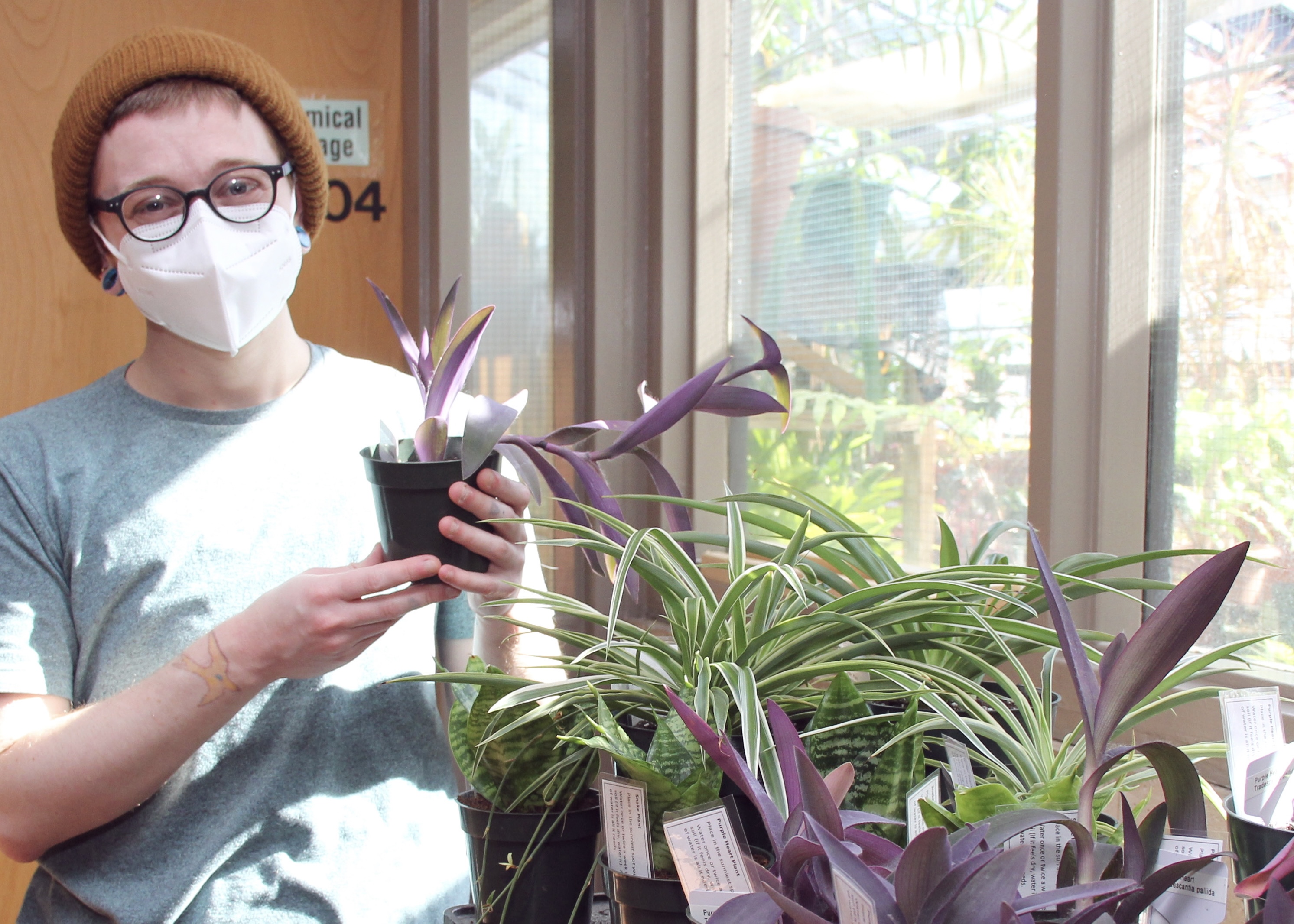 Greenhouse Caretaker Avery Maltz poses with a plant outside of the greenhouse